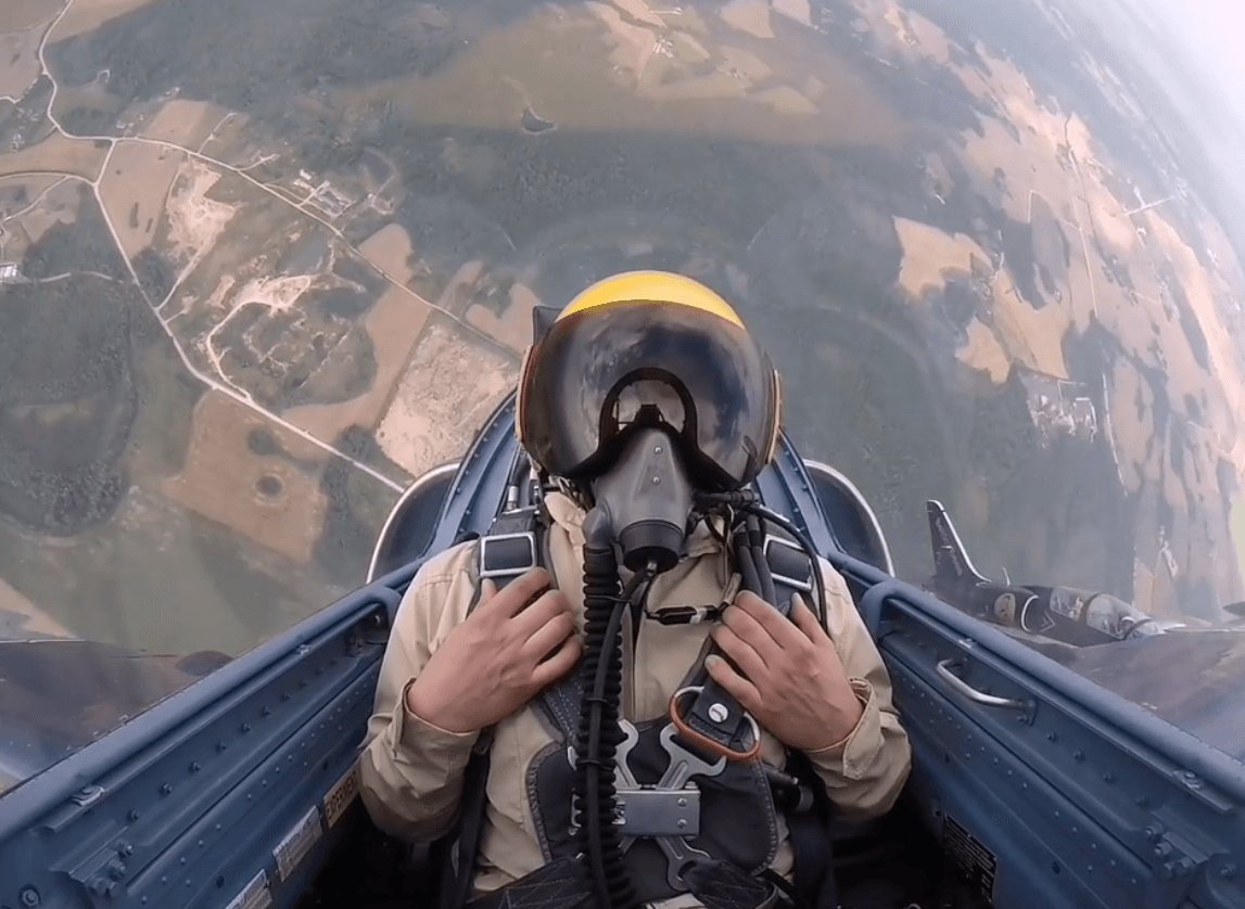 Viljar in a jet cockpit wearing a helmet and oxygen mask, high above farmland